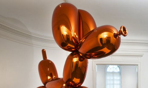 A shiny, orange metal sculpture in the shape of a dog made out of balloons