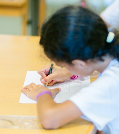 A girl sketches out geometric shapes on a white piece of paper for her kufic calligraphy