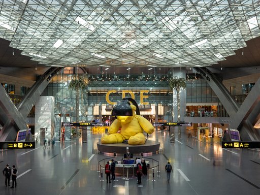A sculpture of a  yellow teddy with a lamp above its head at Hamad International Airport