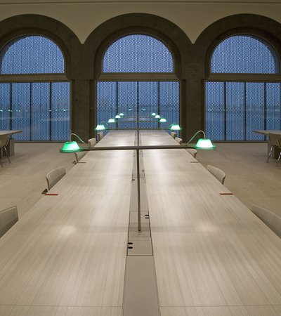 Interior view of MIA's library seating area with three very long tables stretching towards arched windows overlooking Doha city