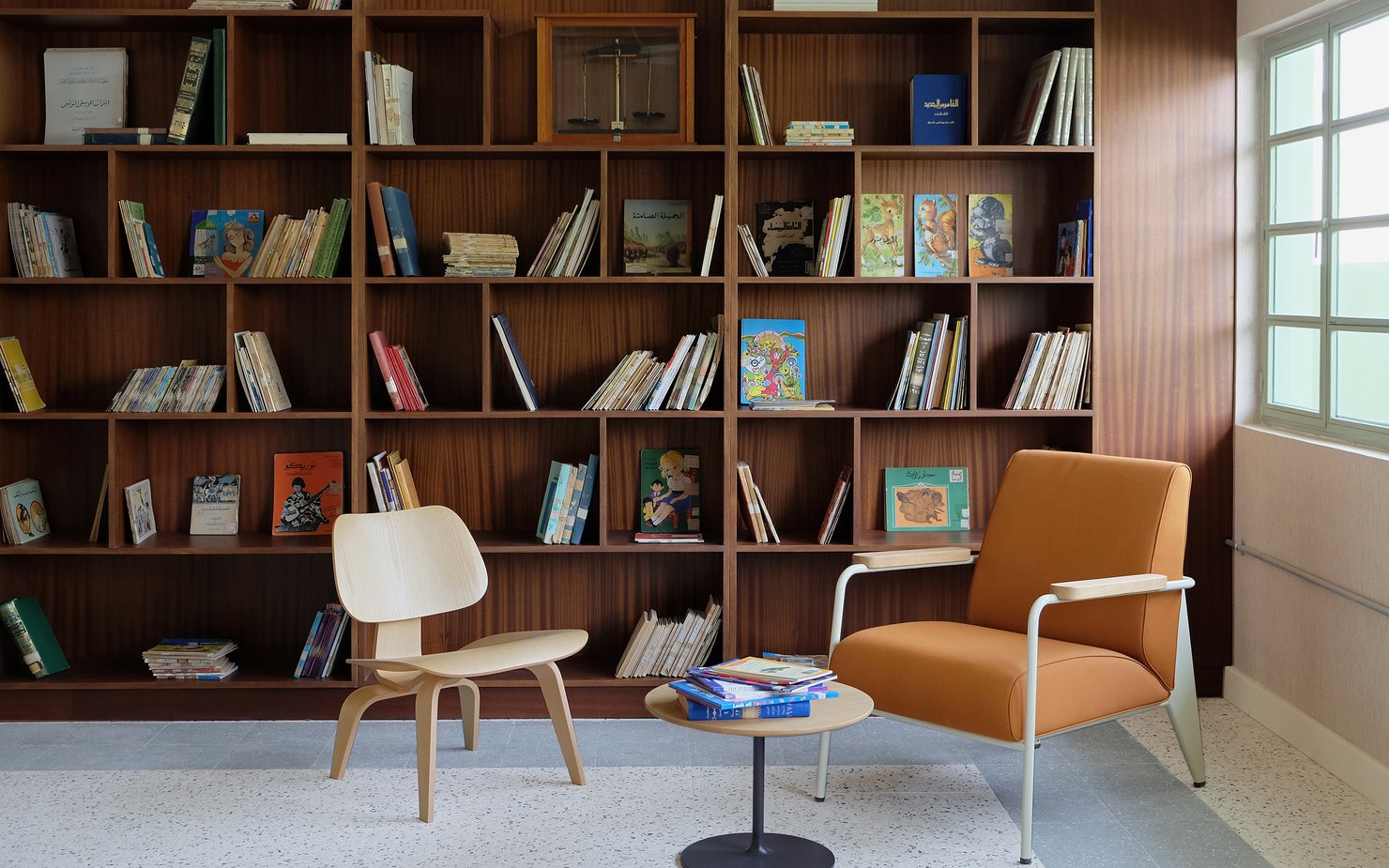 Interior view of a seating area in Liwan's library with two chairs, small table and bookshelves in the background.