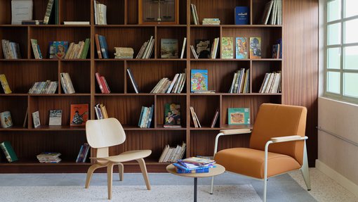 Interior view of a seating area in Liwan's library with two chairs, small table and bookshelves in the background.