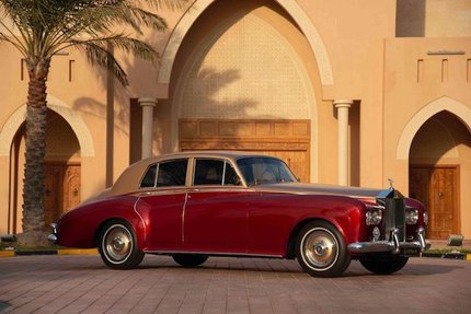 A shot of 1963 vintage Rolls Royce with a bright red sheen and gold details around the bumper and roof