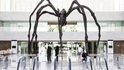 A wide-angle shot showing the full view of the spider sculpture's uniquely sculpted bronze and stainless steel legs