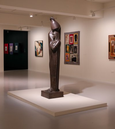 Photo of a gallery space with a sculpture of a peasant women with a jug on her head in the middle.
