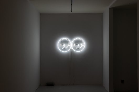 A white neon sign comprised of two white circles with the words 'revolution' and 'prosperity' in Arabic sitting inside the circles.
