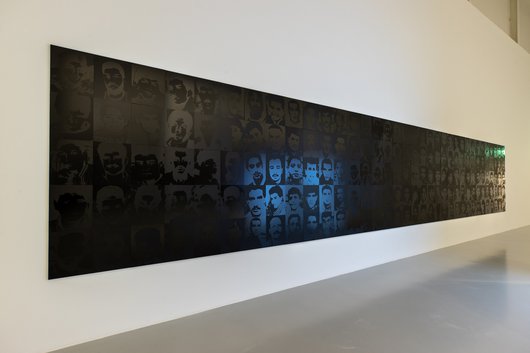 A wall with multiple backlit silkscreen portraits is shown.