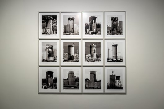 A series of 12 black and white photos of watch towers hung against a white wall.