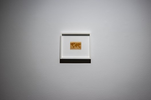 A miniature world map is seen framed by white paper and hung on a white wall.