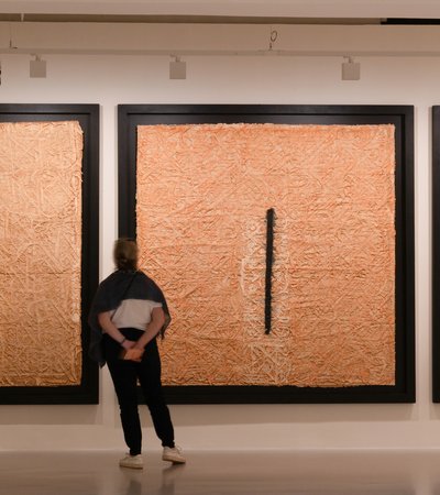 Woman viewing three large, framed, square artworks, textured to look like straw, with black lines.