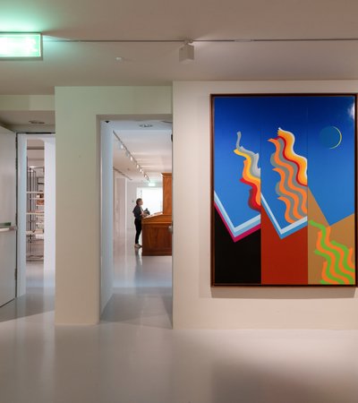 View of a gallery corner, looking through to different spaces, with two artworks hanging in view.