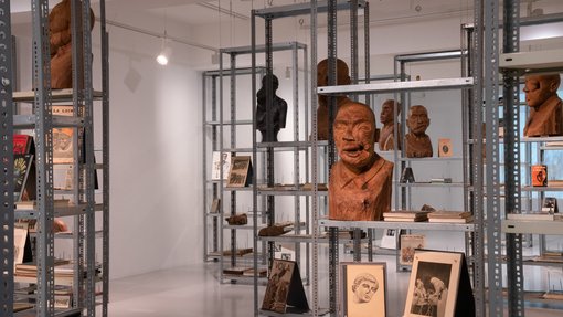 Multiple rust-coloured busts and printed publications are seen displayed on metal cases.