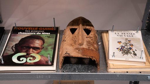 Two publications are seen flanking a wooden-coloured mask.