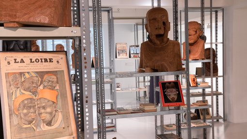 Rust-coloured busts and different publications are displayed on multiple metal cases in a white gallery space.