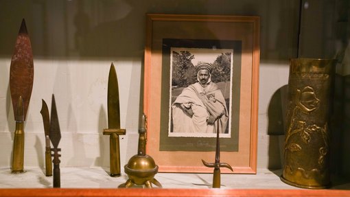 Different sized arrow tips and small daggers on display next to a framed black and white photo of a man in traditional dress.