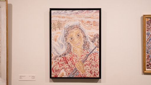 Painting of a woman in a white head covering, hair flowing, holding a rifle, hung against a white wall.