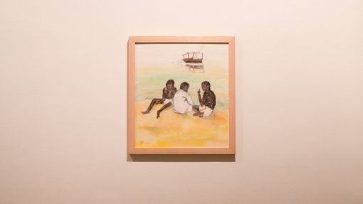 Painting of three boys on a beach with a dhow on the water in the distance, framed and displayed on a white gallery wall.