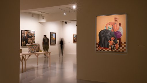 Gallery view of multiple paintings and objects on display with two people viewing the artworks.
