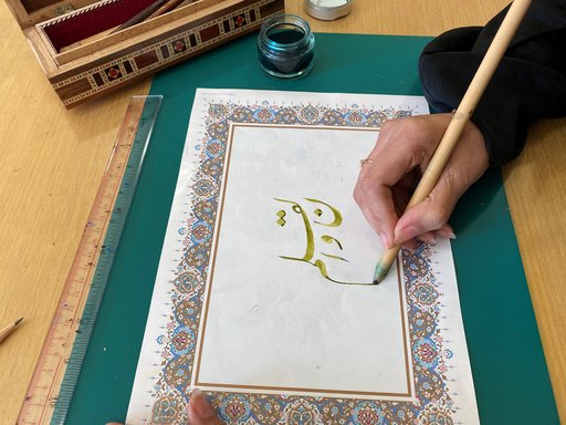 Hand holding a pen and writing in Nasta'liq Script