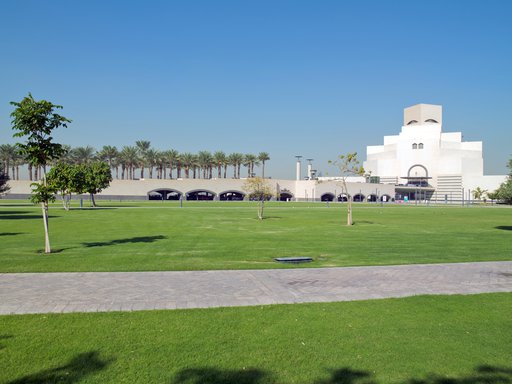 حديقة مفتوحة تتضمن عشباً أخضر وأشجاراً محلية ويظهر في الخلف مبنى متحف الفن الإسلامي