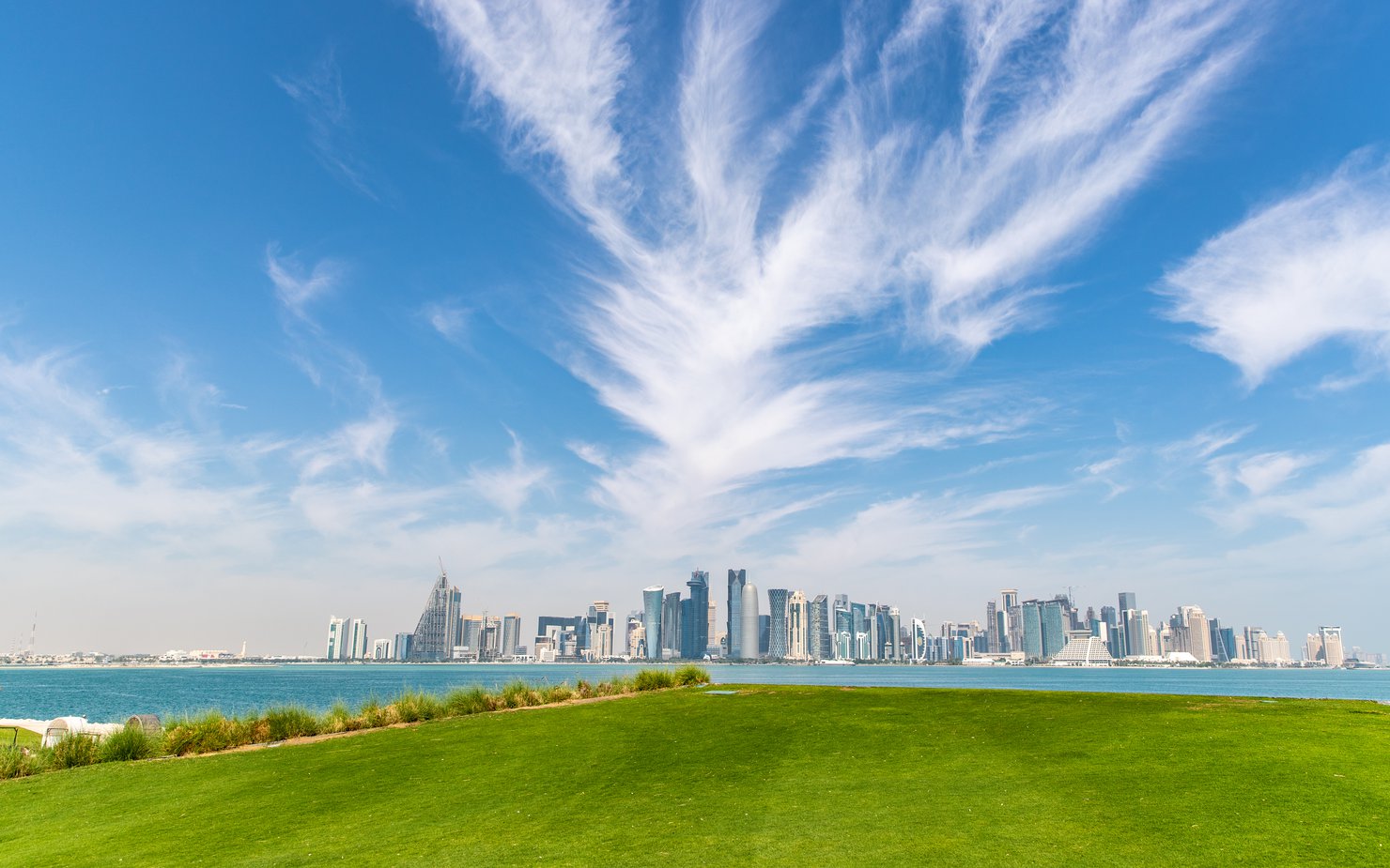 A panorama of Doha's skyline behind a large green grassy area