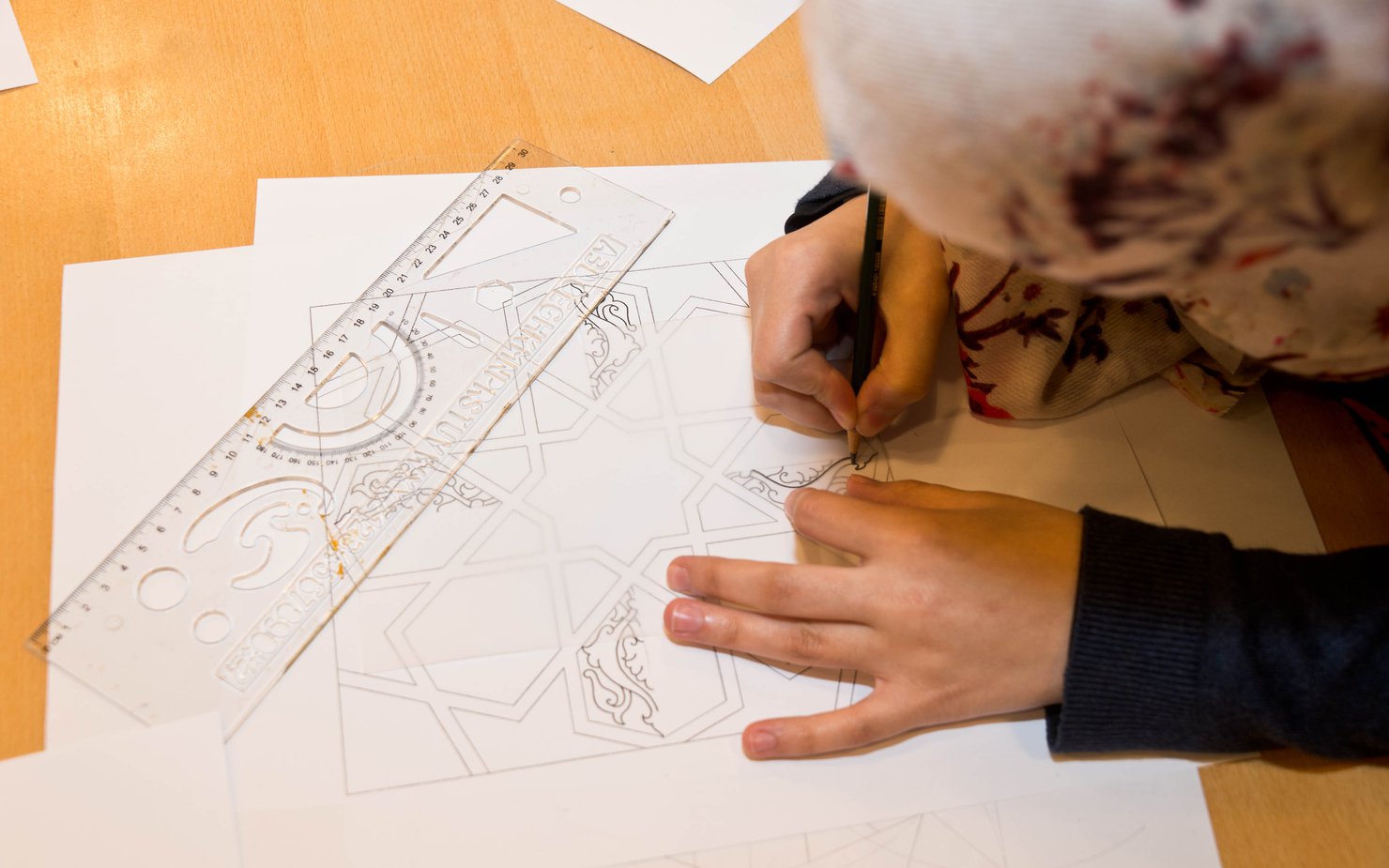 Bird's-eye view of a girl sketching out Islamic art patterns on a piece of white paper