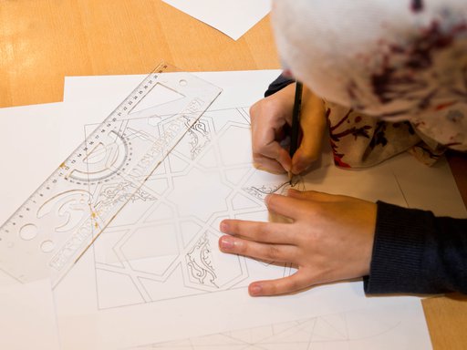 Bird's-eye view of a girl sketching out Islamic art patterns on a piece of white paper