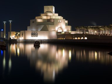 View of the Museum of Islamic Art illuminated at nighttime with its reflection in the surrounding water