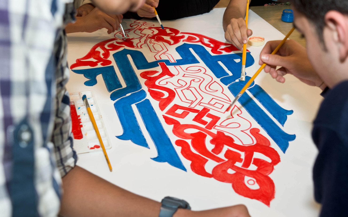 A group of workshop attendees use blue and red paint to color large calligraphy letters