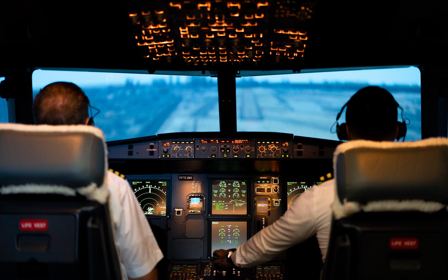 Two pilots sit in the cockpit of a plane navigating through a field