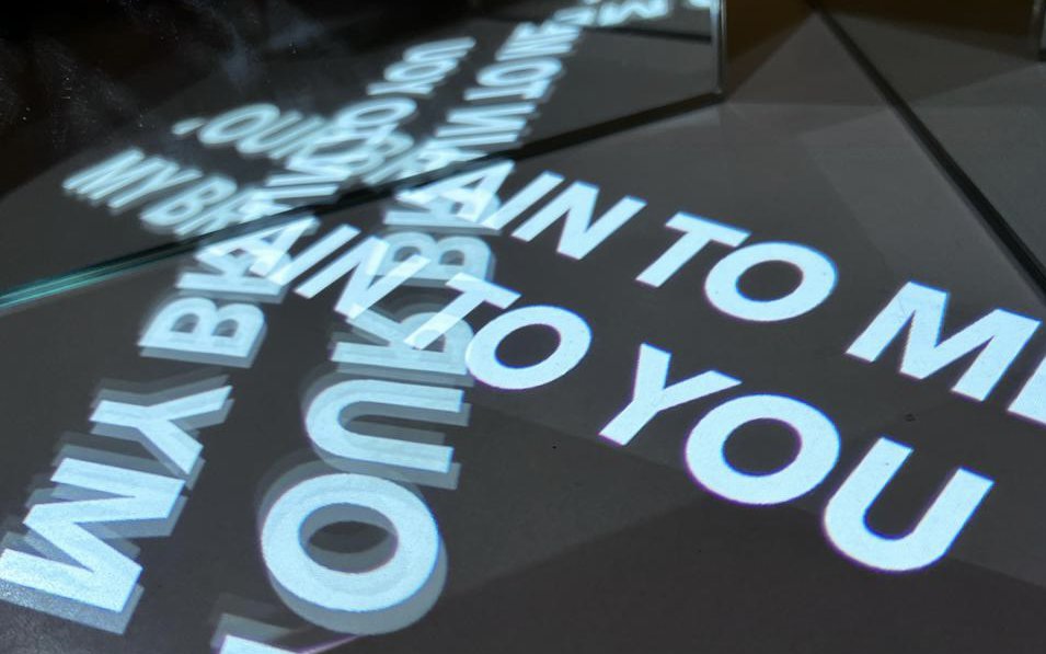 Projection of the phrase 'my brain to you' reflected against the floor and mirror