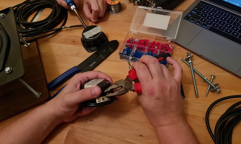 Two people working with pliers and cables alongside other tools and a laptop