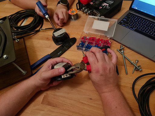 Two people working with pliers and cables alongside other tools and a laptop