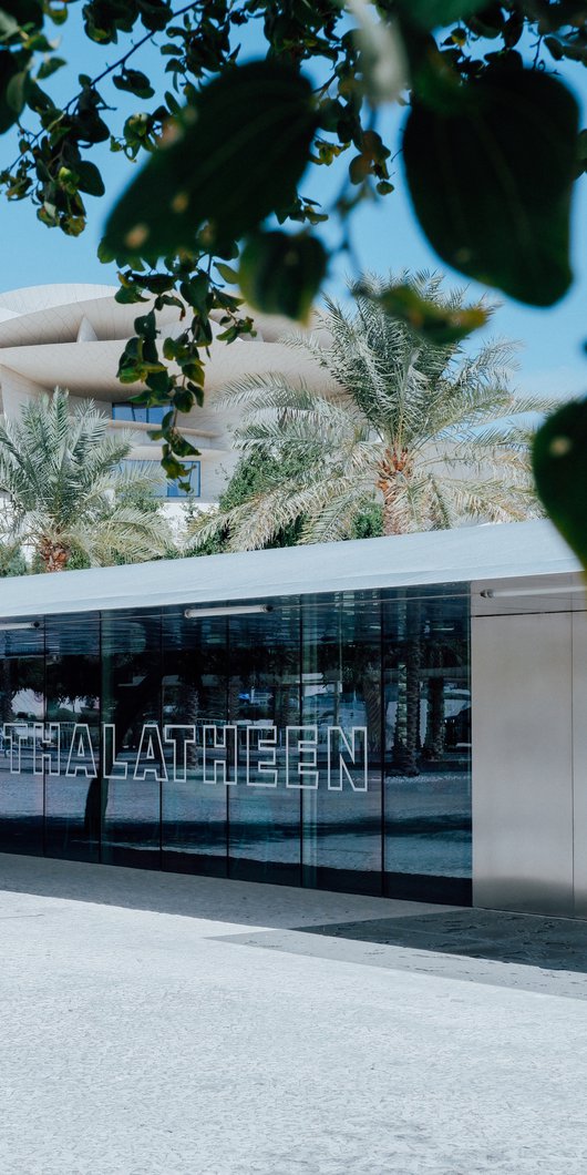An exterior view of Thalatheen Cafe with the National Museum of Qatar in the background