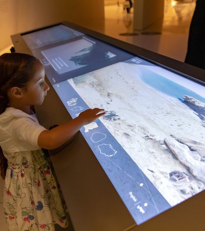 A little girl interacting with a digital gallery display at the National Museum of Qatar.