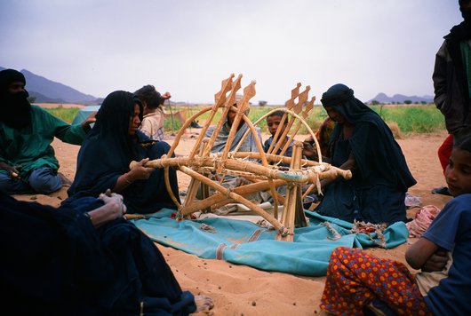 Women preparing a saddle for their camel, surrounded by a number of men and children