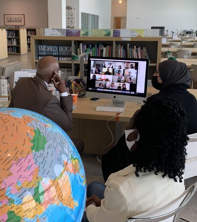 A man and a woman in a library talking to children via online video call with a globe present in the foreground of the image