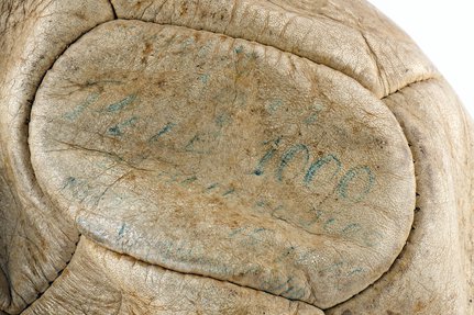 Faded blue writing on an aged leathery football reads 'Pele 1000'.
