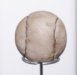 A white leather golf ball with visible sewing lines rests on a metal display.