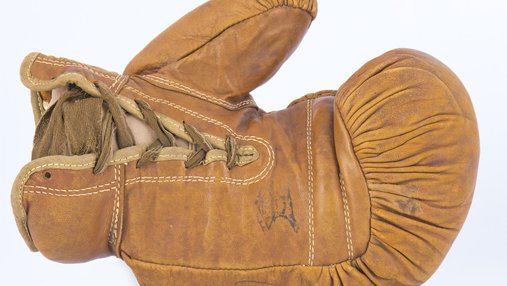 A camel coloured, aged, leather boxing glove lies on its side.