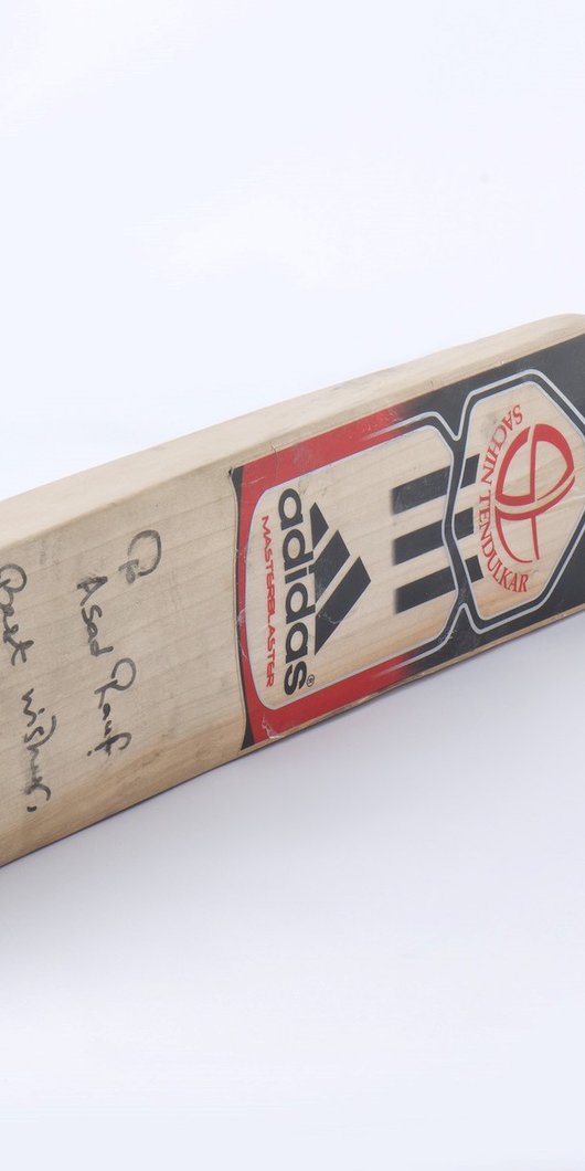 An Adidas Master Blaster cricket bat with the name Sachin Tendulkar and a signed dedication that says "To Asad Rauf, Best Wishes, Sachin Tendulkar"