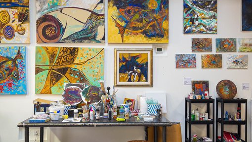 استوديو الفنانة الرائدة وفيقة سلطان العيسى في مطافئ، لوحاتها على الحائط، وطاولة عليها مستلزمات فنية.