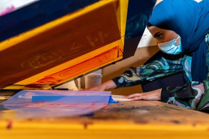 A woman leans over her colourful screen print.
