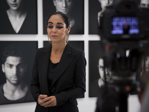Portrait of the artist Shirin Neshat standing in Mathaf: Arab Museum of Modern Art, while being interviewed alongside a backdrop of her art