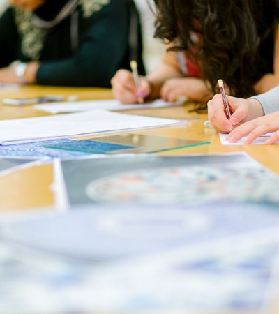 A shot of workshop participants sketching with pencils with scattered paper on the table.