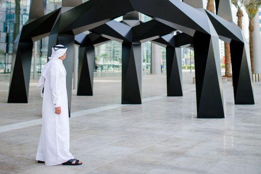 A man in traditional Qatari attire looking up at Tony Smith's life-size art piece, Smoke