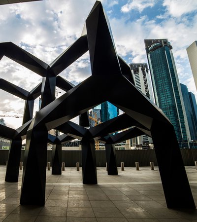 A view of Smoke, a black metal geometric sculpture by Tony Smith set against a backdrop of tall buildings in Doha