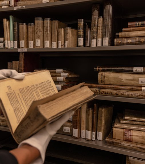 Person wearing white gloves and holding an antique book in front of library book shelves at the Museum of Islamic Art, Qatar