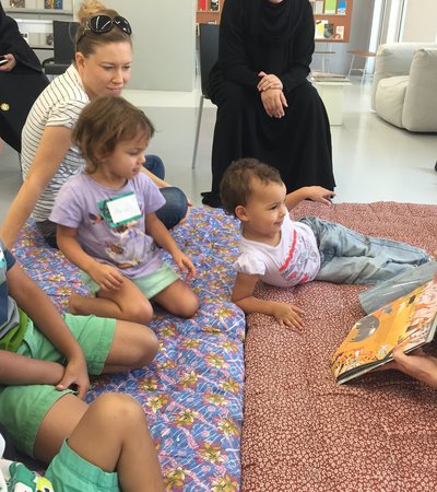 A group of young children and their parents gather while a lady reads a story to them