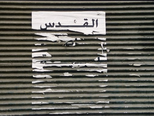 Picture of shredded paper on a textured background with the word Al Quds in Arabic